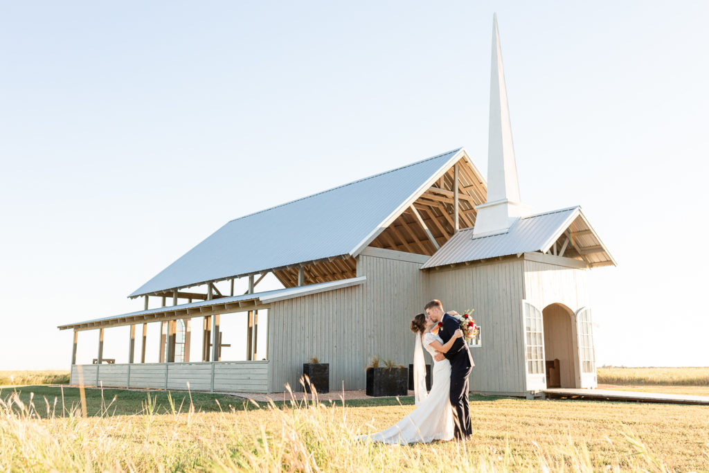 A sunset portrait of a bride and groom kissing in front of the Allen Farmhaus, one of the best austin wedding venues. 