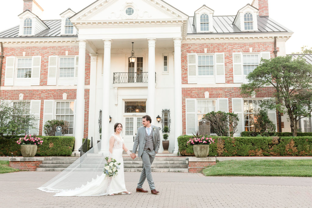 A bride and groom walking and smiling at the Texas Federation of Women's Club (TFWC) Mansion, one of the best austin wedding venues. 